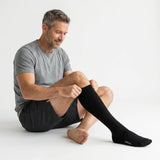 Man pulling on Velora Original black compression sock